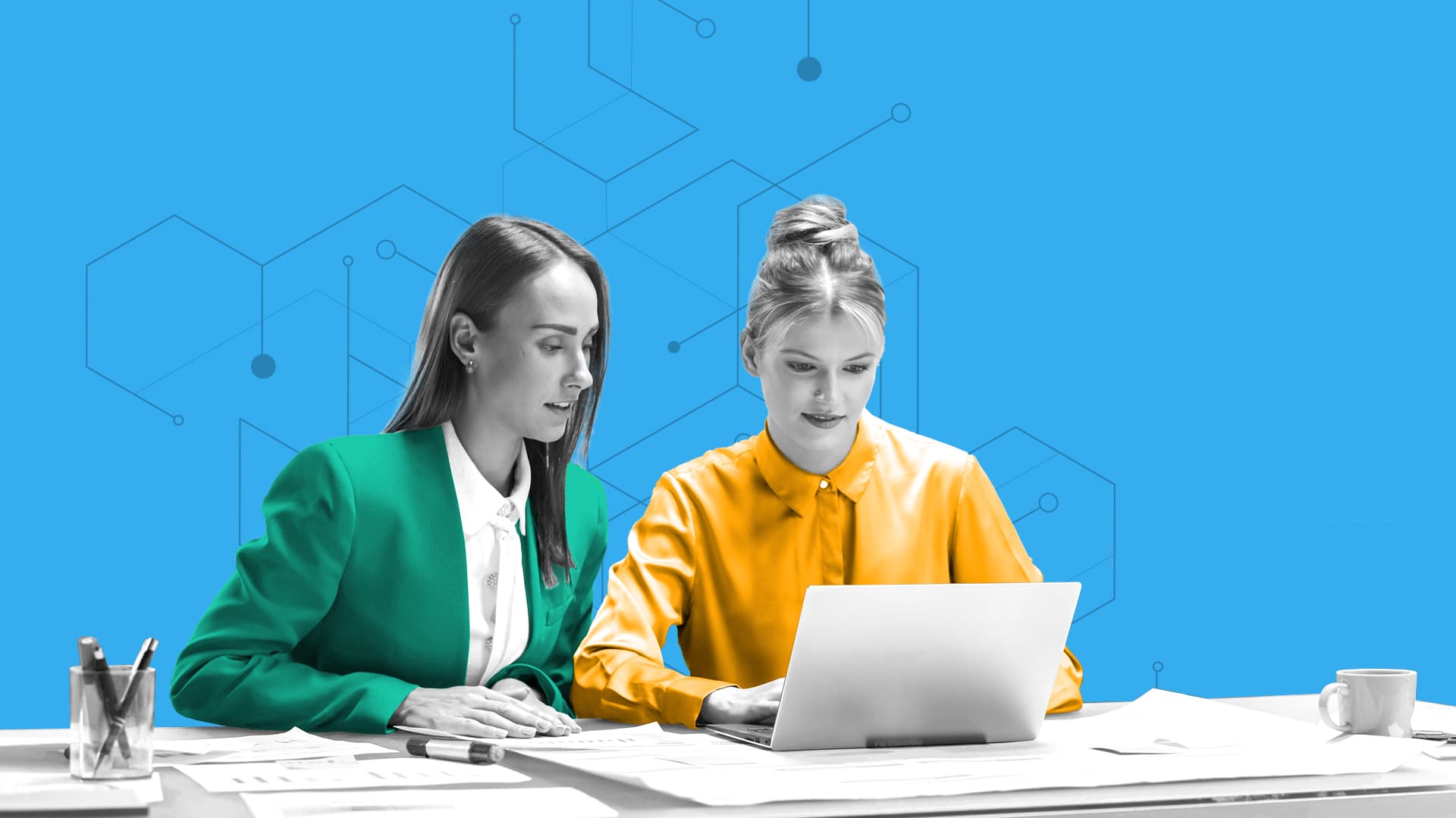This image features two people sitting next together at a desk, one is wearing a green blazer, the other a yellow top. On the desk, there are papers and a computer.