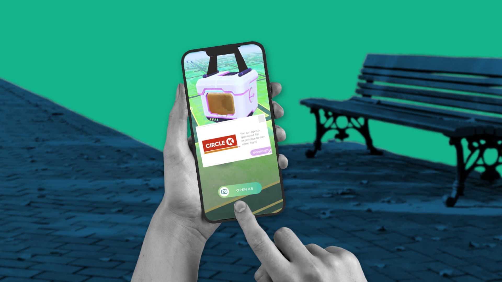 This image features someone in a park. You can see their hand with a smartphone in it. Behind that, there is a park bench. On the phone, you can see an example of an in-game advertisement.