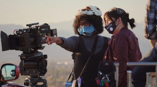 An image of a woman of color directing a scene, with camera and crew